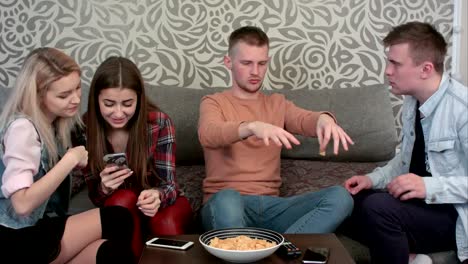 Happy-casual-young-female-friends-laughing-at-what-they-see-on-a-cell-phone,-while-their-male-friends-are-talking