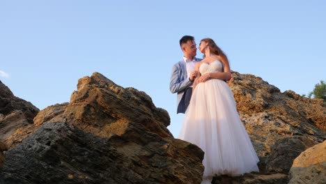 Beautiful-young-wedding-couple-standing-on-sea-shore-with-rocks.-Newlyweds-spend-time-together:-embrace,-kiss-and-care-for-each-other.-Love-concept