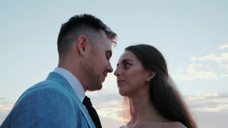 Beautiful-young-wedding-couple-standing-on-sea-shore-with-rocks.-Newlyweds-spend-time-together:-embrace,-kiss-and-care-for-each-other.-Love-concept.-Bride-smiling-to-groom