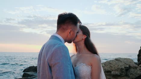 Beautiful-young-wedding-couple-standing-on-sea-shore-with-rocks.-Newlyweds-spend-time-together:-embrace,-kiss-and-care-for-each-other.-Love-concept