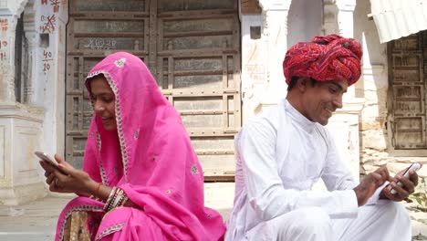 Pan-down-to-a-couple-in-Rajasthani-traditional-dress-busy-ignoring-on-their-own-cell-phones,-hectic-separate-lifestyle