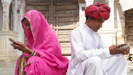 Couple-busy-on-their-own-smart-phones-laughing-and-smiling-and-their-back-turned-away-towards-each-other