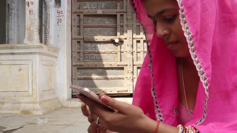 Neigung-bis-zu-einer-indischen-Ethnizität-Frau-in-Rosa-Saree-beschäftigt-auf-ihrem-Smart-phone-beobachten-Chat-video-Internet