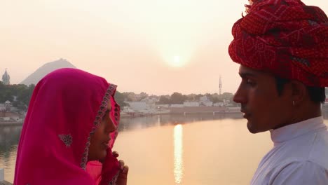 Husband-and-wife-talking-against-the-beautiful-sunset-at-Pushkar-Lake,-India,-handheld