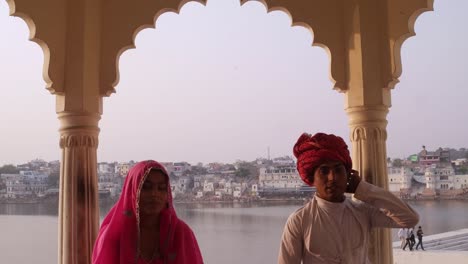 Tilt-down-to-attractive-Indian-couple-in-traditional-dress-with-Pushkar-lake-in-the-background,-Rajasthan,-India