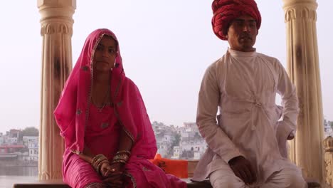 Hermosa-pareja-indio-en-traje-tradicional-sentado-con-el-lago-de-Pushkar-en-el-fondo,-Rajasthan,-India