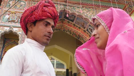 Hermosa-mujer-en-sari-rosa-y-atractivo-hombre-de-turbante-rojo-fuera-de-un-templo-de-Pushkar,-Rajasthan,-India