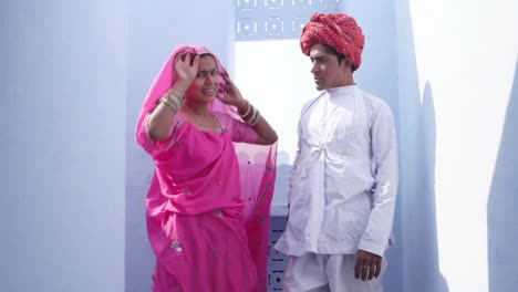 Woman-in-pink-sari-walks-upto-a-man-in-red-turban-and-white-kurta-and-pose-for-camera-in-Rajasthan,-India