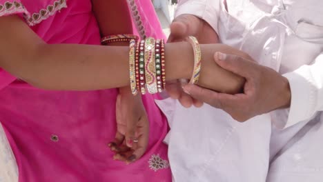 Traditionelle-indische-Braut-mit-rosa-Sari-Multi-farbige-Armbänder-sitzt-mit-ihrem-Mann-mit-einer-Ansicht-des-Karnevals-in-der-Kulisse-in-Rajasthan-in-Pushkar-Mela