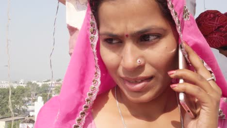 Woman-in-pink-sari-talking-and-chatting-on-cell-phone-talking,-ignoring-the-man-behind-her-in-red-turban-in-India