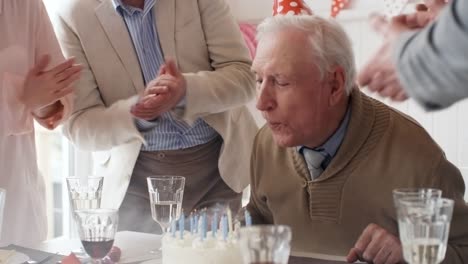 Elderly-Man-Blowing-Off-Candles-at-Birthday-Dinner-Party