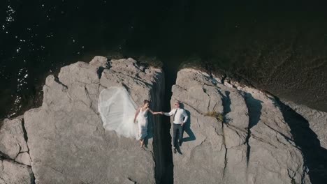 Young-and-beautiful-wedding-couple-lie-together-on-the-mountain-and-hold-hands-of-each-other.-Shooting-from-the-air.-Aerial-shot.-Lovely-groom-and-bride