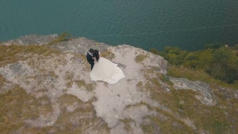 Joven-y-hermosa-pareja-junto-en-la-ladera-de-la-montaña-cerca-del-mar.-Hermoso-novio-y-novia.-Disparos-desde-el-aire.-Toma-aérea