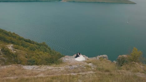 Joven-y-hermosa-pareja-junto-en-la-ladera-de-la-montaña-cerca-del-mar.-Hermoso-novio-y-novia.-Disparos-desde-el-aire.-Toma-aérea