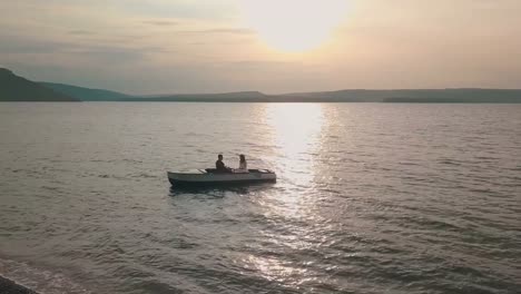 Joven-y-hermosa-pareja-junto-navegando-en-un-barco-con-remos-en-el-mar.-Puesta-de-sol.-Hermoso-novio-y-novia.-Disparos-desde-el-aire.-Toma-aérea