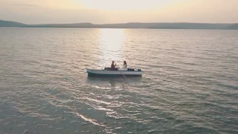 Joven-y-hermosa-pareja-junto-navegando-en-un-barco-con-remos-en-el-mar.-Puesta-de-sol.-Hermoso-novio-y-novia.-Disparos-desde-el-aire.-Toma-aérea