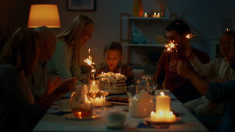 Birthday-Celebration-of-Cute-Little-Girl-at-the-Dinner-Table,-Mother-Brings-Cake-and-Girl-Blows-Out-Candles.-At-the-Table-Happy-Relatives-and-Friends-Gathered-To-Celebrate.