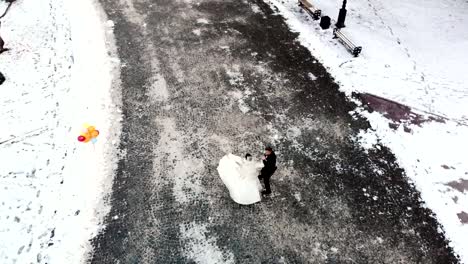 winter-wedding.-Aerial-view-of-newlywed-couple-in-wedding-dresses-are-dancing-wedding-dance-in-a-snow-covered-park,-against-the-background-of-ancient-architecture-and-paving-stones