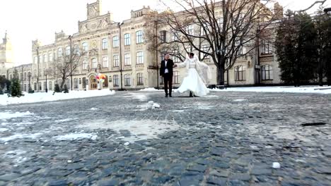 Winter-Hochzeit.-Brautpaar-in-Brautkleider-sind-Fuß-durch-den-tief-verschneiten-Park,-vor-dem-Hintergrund-der-antiken-Architektur-und-Pflastersteine