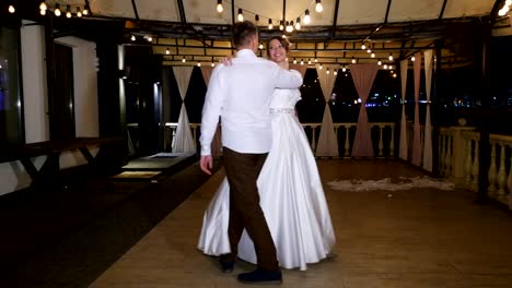 noche-de-invierno,-una-terraza-decorada-con-focos-de-luz,-en-la-calle,-los-novios-están-bailando-su-primer-baile-de-boda,-un-vals.-boda-de-invierno