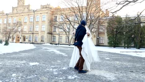 winter-wedding.-newlywed-couple-in-wedding-dresses-are-dancing-wedding-dance-in-a-snow-covered-park,-against-the-background-of-ancient-architecture-and-paving-stones