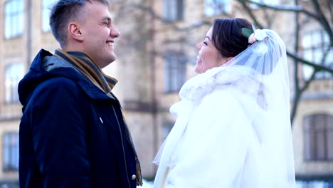 Winter-Hochzeit.-Brautpaar-in-Brautkleidern.-Bräutigam-küsst-die-Braut-sanft-auf-die-Stirn,-umarmen.-Sie-sind-glücklich,-Lächeln-einander-an.-Hintergrund-der-antiken-Architektur,-tief-verschneiten-park