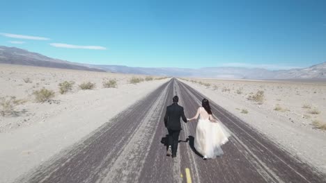 Bride-and-groom-running-on-empty-desert-road-at-Death-Valley,-USA