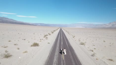 Bride-and-groom-running-on-empty-desert-road-at-Death-Valley,-USA