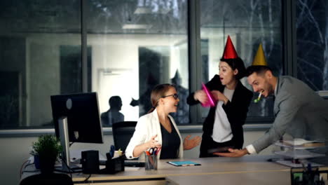 Bonita-rubia-está-trabajando-en-la-oficina-moderna-cuando-sus-colegas-están-trayendo-la-torta-de-cumpleaños,-gorros-de-fiesta-y-presente,-chica-es-abrir-la-caja-de-regalo-y-disfrutar-Felicidades