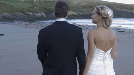 Sonriente-pareja-de-recién-casados-caminando-por-la-playa