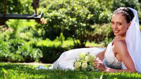 Pretty-bride-smiling-at-camera-lying-on-the-grass