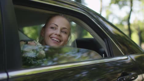 Young-beautiful-happy-bride-sits-in-a-car-and-waves-out-of-the-window.