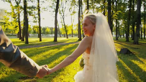 Smiling-bride-holds-groom-by-the-hand-and-runs-in-a-park.