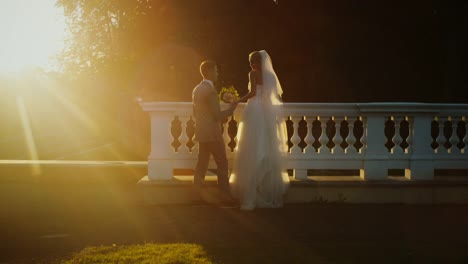 Braut-und-Bräutigam-schauen-sich-den-Sonnenuntergang-von-einem-Balkon-in-einem-Park-aus-an.