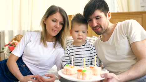 Familia-sonriente-celebrando-su-cumpleaños-hijo-juntos-antes-de-soplar-velas-en-el-pastel