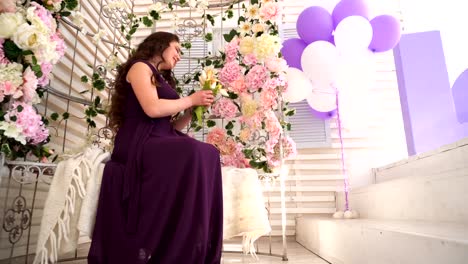 Young-woman-in-purple-dress-sits-on-wedding-bench-with-flowers