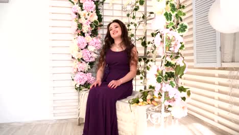 Young-woman-in-purple-dress-sits-on-wedding-bench-with-flowers