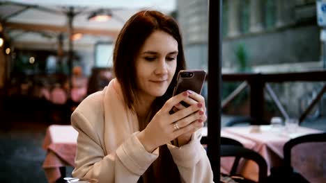 Mujer-hermosa-joven-sentado-en-el-café-de-noche-y-con-el-smartphone.-Hermosa-mujer-navegando-en-Internet