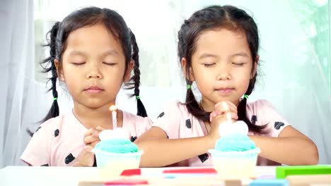 Twin-two-asian-girls-make-folded-hand-to-wishing-the-good-things-for-their-birthday.-Dolly-shot-in-studio.