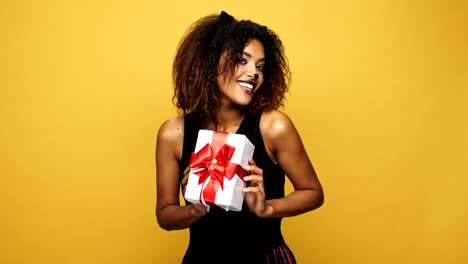 Young-happy-african-woman-cat-with-pretty-make-up-shaking-present-and-smiling-isolated-over-yellow