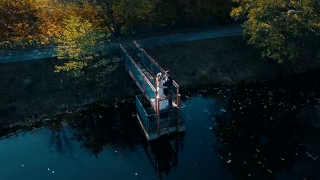 Pareja-joven-está-de-pie-sobre-un-pequeño-puente-cerca-del-lago-hermoso