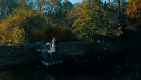 Pareja-joven-está-de-pie-sobre-un-pequeño-puente-cerca-del-lago-hermoso