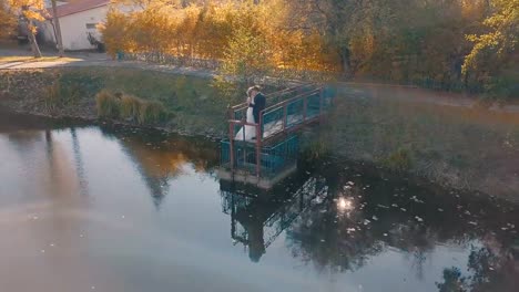 Pareja-joven-está-de-pie-sobre-un-pequeño-puente-cerca-del-lago-hermoso