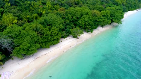 Aerial:-A-couple-walks-along-the-beach-with-white-sand-and-turquoise-water.