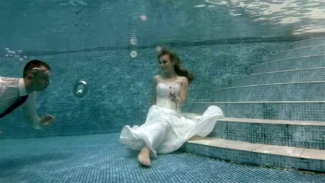 4K-The-groom-swims-underwater-to-the-bride-that-sits-at-the-bottom-of-the-pool-and-kisses-her-hand