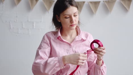 Professional-woman-florist-unwinds-the-red-ribbon,-cuts-it-with-scissors-to-pack-the-bouquet