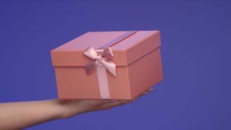 Womans-Hand-holding-a-lovely-Gift-Box-on-Bluescreen;-Celebration-Concept