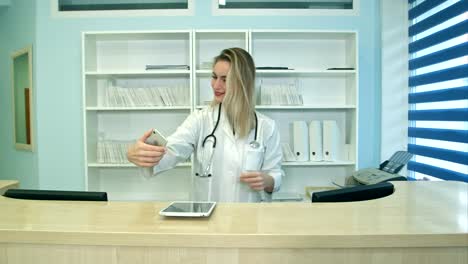 Smiling-female-medical-worker-taking-selfies-with-her-phone-at-reception-desk