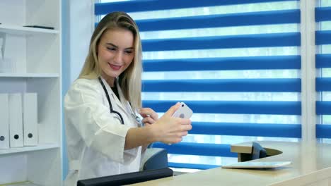 Smiling-nurse-taking-selfies-with-her-phone-behind-reception-desk