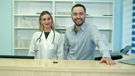 Friendly-male-and-female-nurses-behind-reception-desk-in-hospital